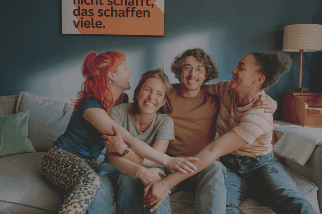 Jungen Menschen (Mitglieder) sitzen auf dem Sofa und umarmen sich.