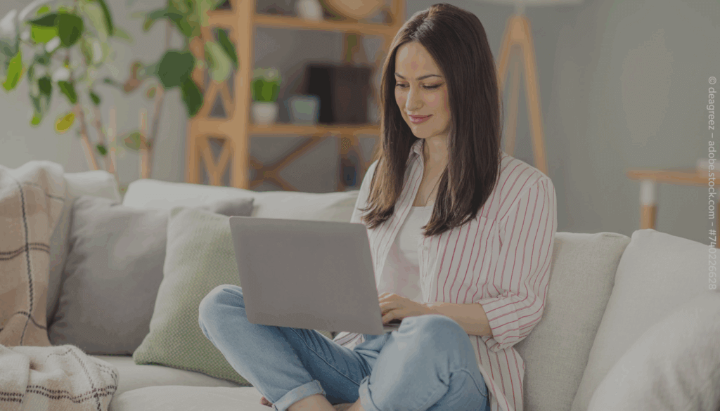 Frau sitzt auf dem Sofa und hat einen Laptop auf dem Schoß.
