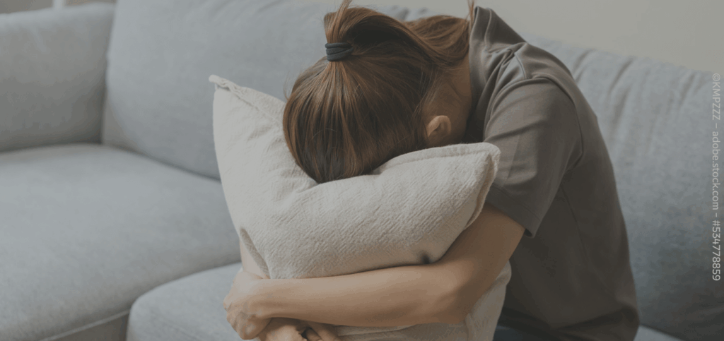 Eine Frau sitzt auf dem Sofa und vergräbt ihren Kopf in einem Kissen.
