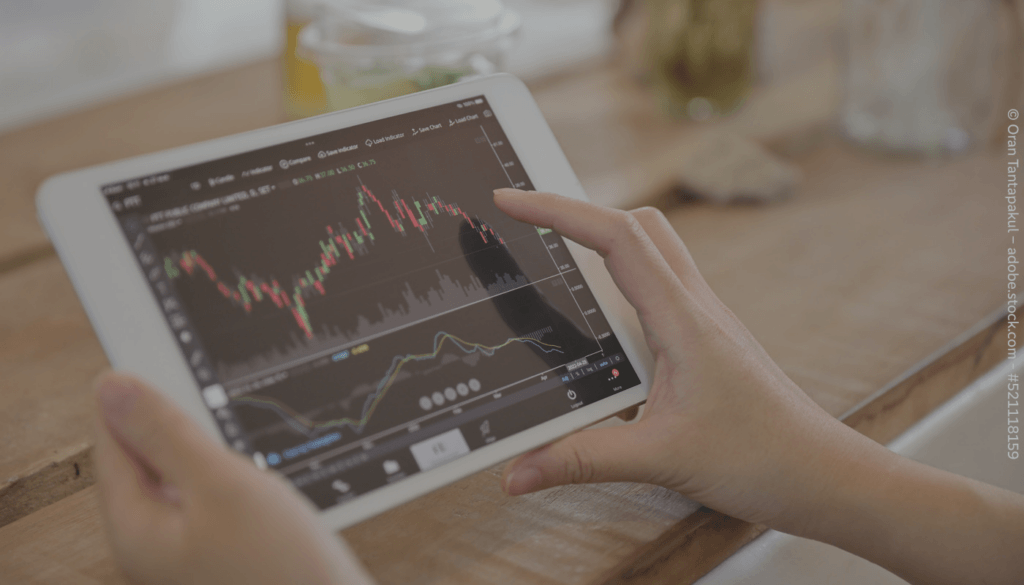 Jemand hält ein Tablet in den Händen, auf dem ein schwankender Börsenkurs angezeigt wird.